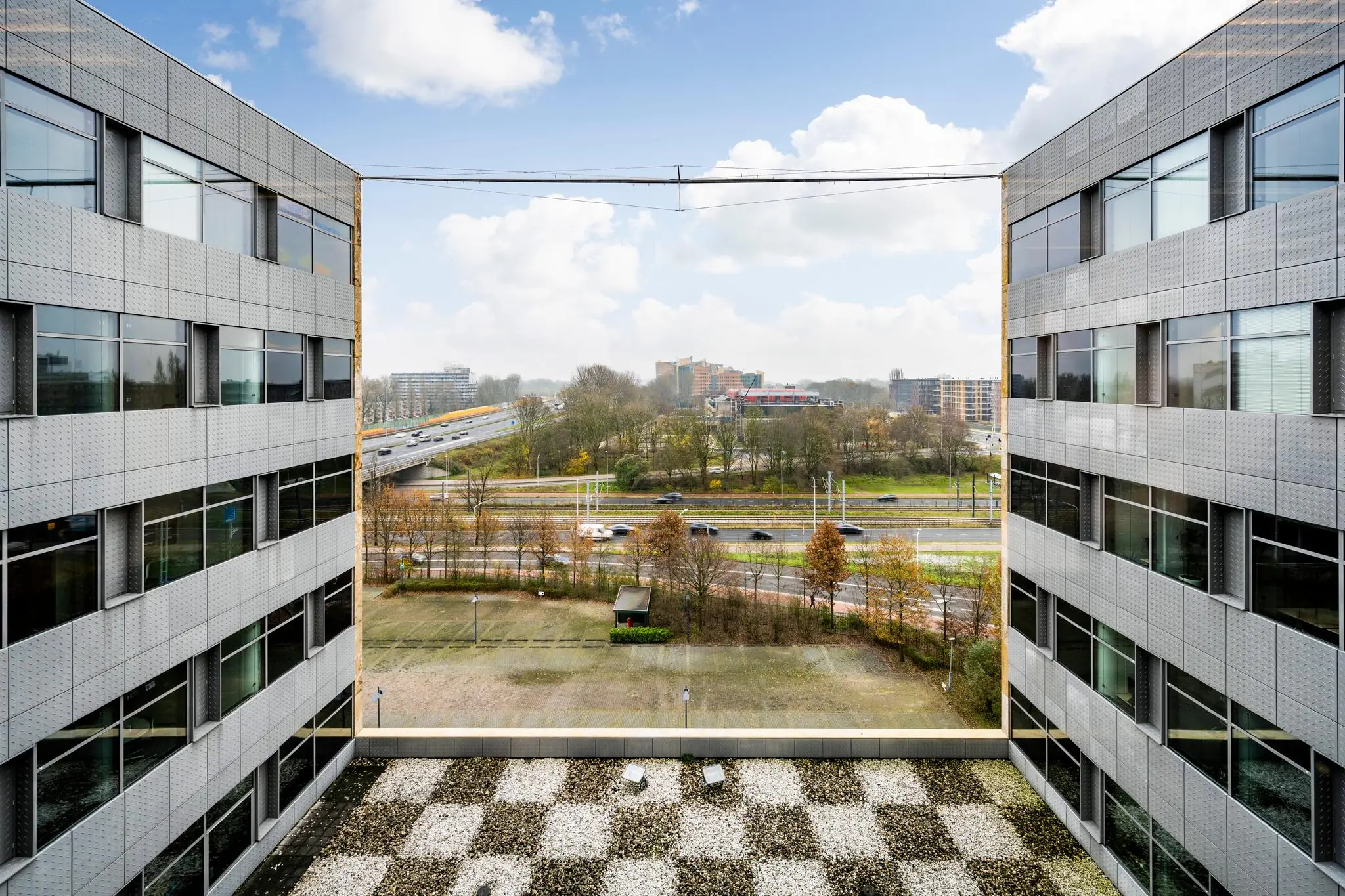 Uitzicht vanaf een modern kantoorgebouw aan de Burgemeester Rijnderslaan op een snelweg, spoorlijn en stedelijke omgeving.